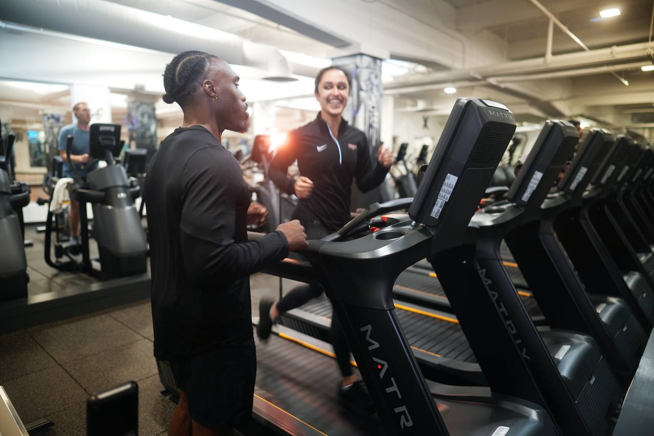 Udoka beside a client on a treadmill, both laughing